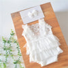 White lace baby romper with matching headband laid on a wooden surface.