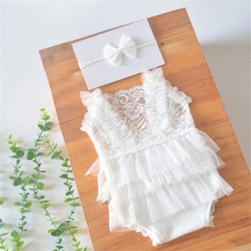 White lace baby romper with matching headband laid on a wooden surface.