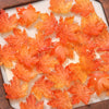 Orange maple leaf glass beads arranged on a white surface for DIY jewelry making
