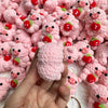 A hand holds a cluster of handmade crochet mini pig keychains in various shades of pink and red.