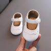 A hand holds a white lace-trimmed baby girl moccasin shoe with a bow, showing the interior and exterior detail.