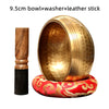 A hammered copper singing bowl with a washer and leather stick resting on a red fabric base.