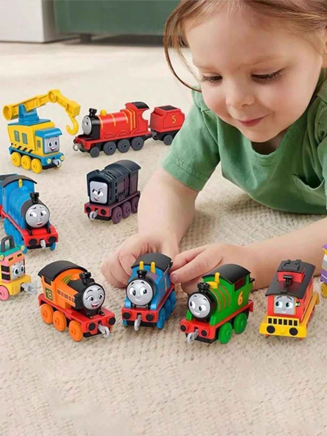 A young child is interacting with various Thomas & Friends diecast train toys on a light-colored carpet.