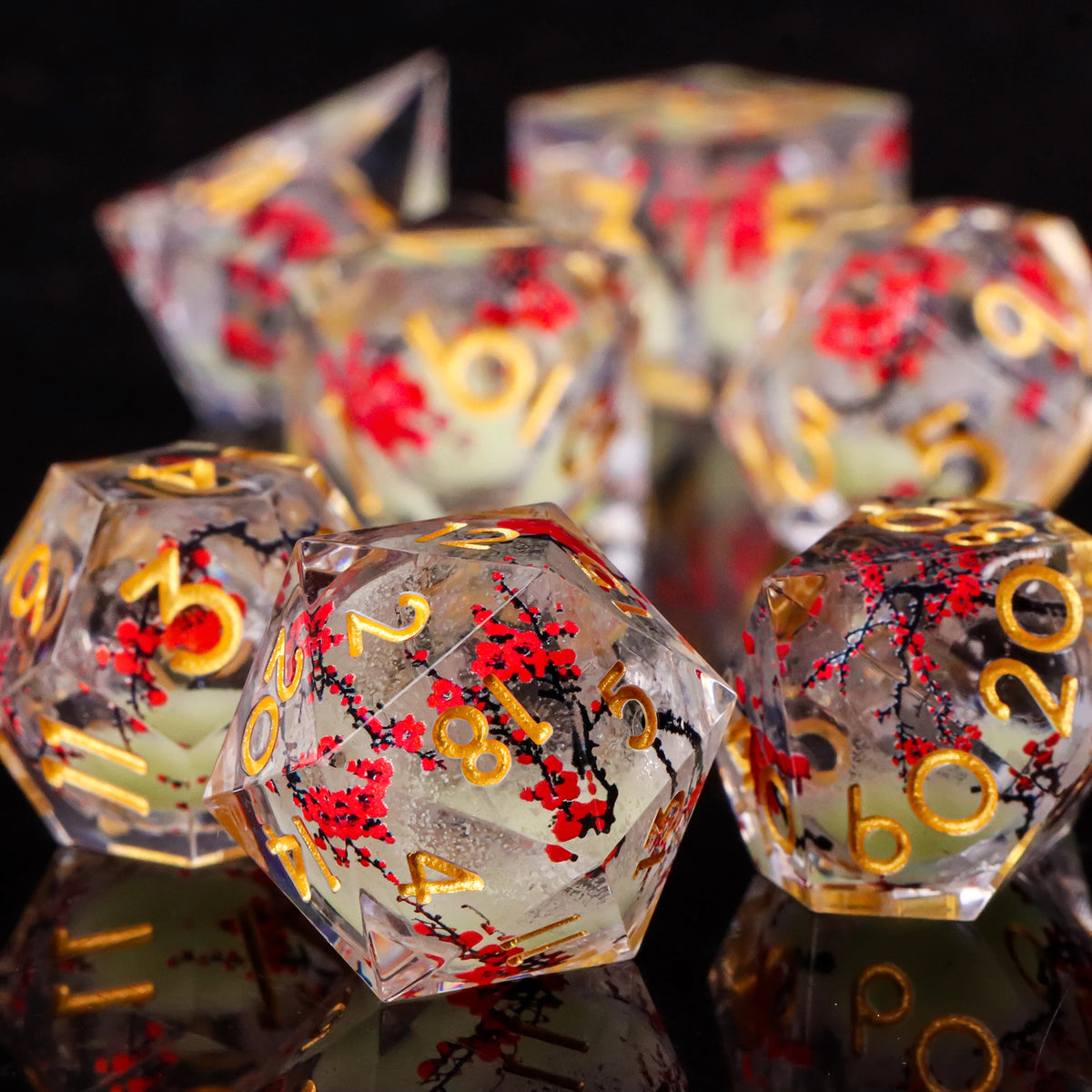 A close-up of a set of translucent resin dice with red plum blossoms and gold accents, reflecting on a dark surface.