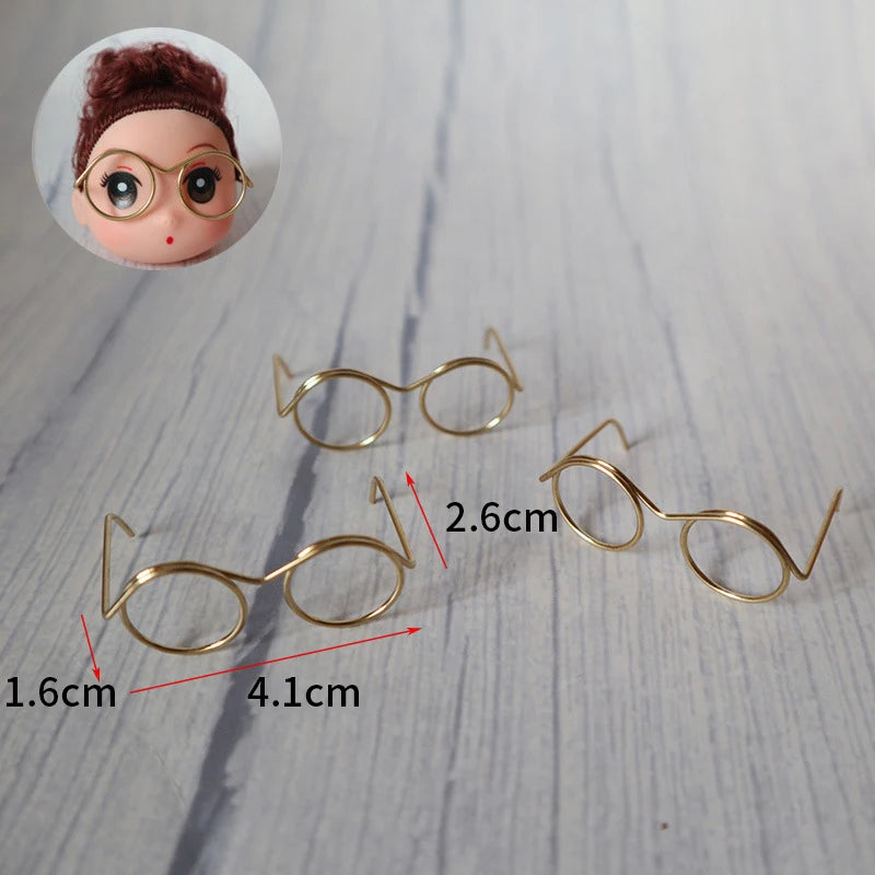 A set of five metal round glasses frames for dolls shown on a light wooden surface.