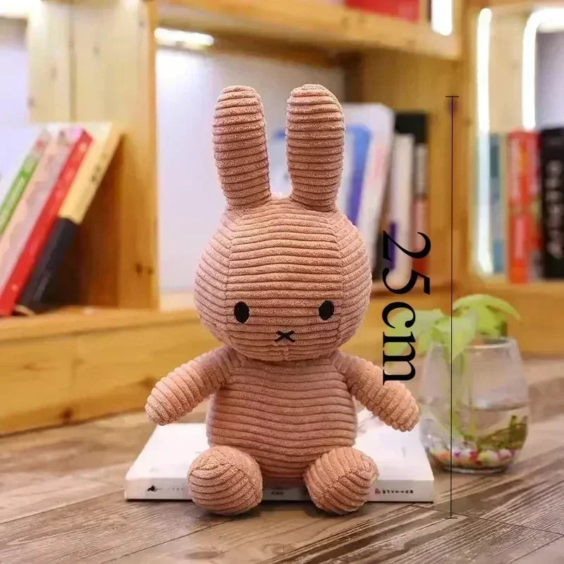 A soft, light brown Miffy plush toy resembling a rabbit is displayed on a wooden surface.