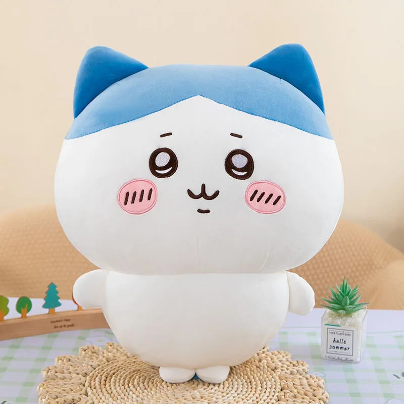 A white and blue Chiikawa plush doll with large eyes sitting on a textured surface.