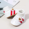 White baby booties with red stripes and tan accents shown on a light background.