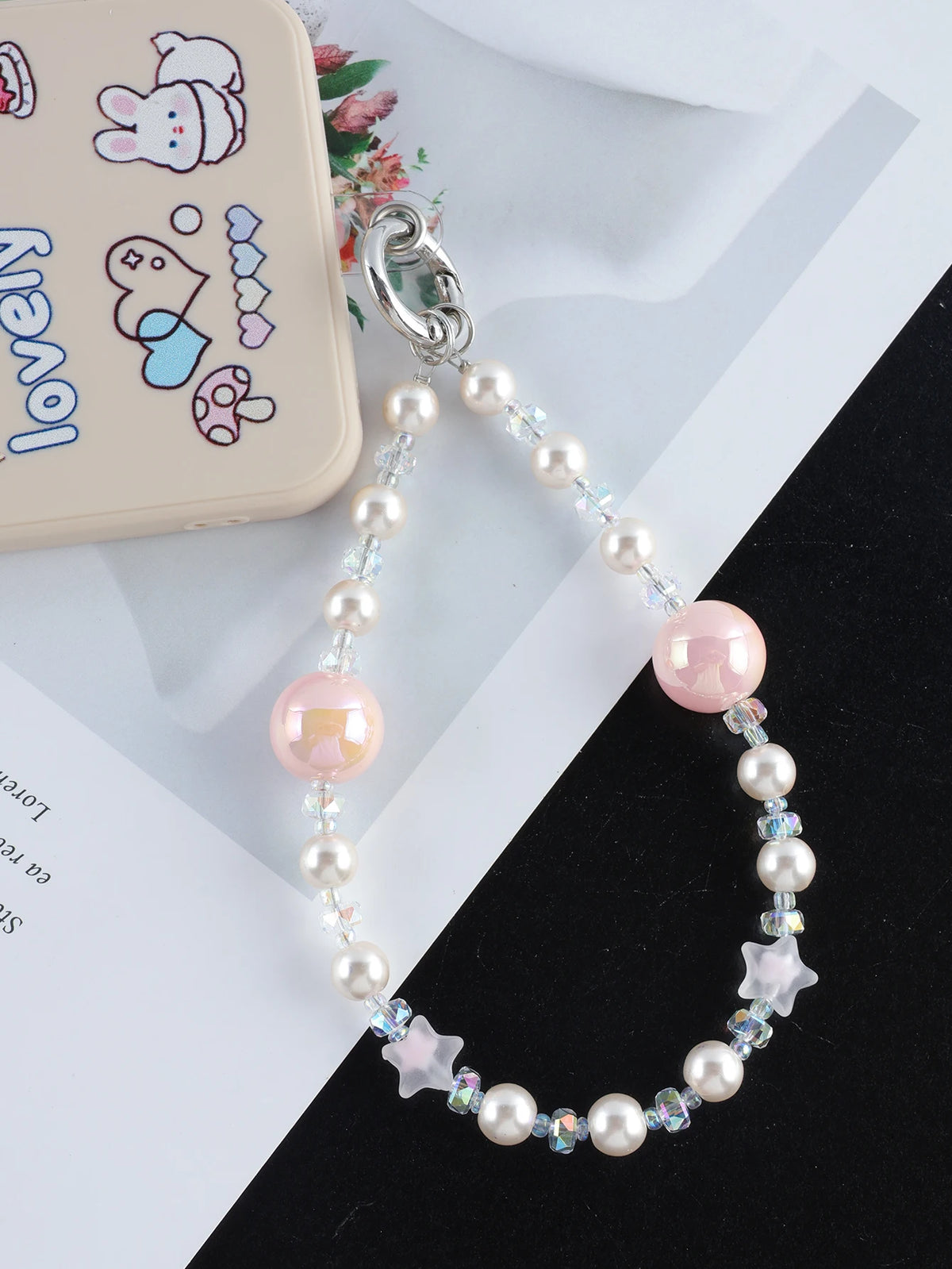 A silver necklace featuring pink and clear pearl crystals and star charms, displayed next to a phone case.