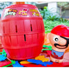 A red pirate barrel game with a sword stab piece and a small plastic pirate figure on a wooden surface.