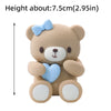 A cute, light brown teddy bear cake topper with blue accents and a bow.