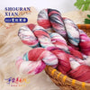 A bundle of hand-dyed wool yarn in pink, blue, and white gradients is displayed in a woven basket.