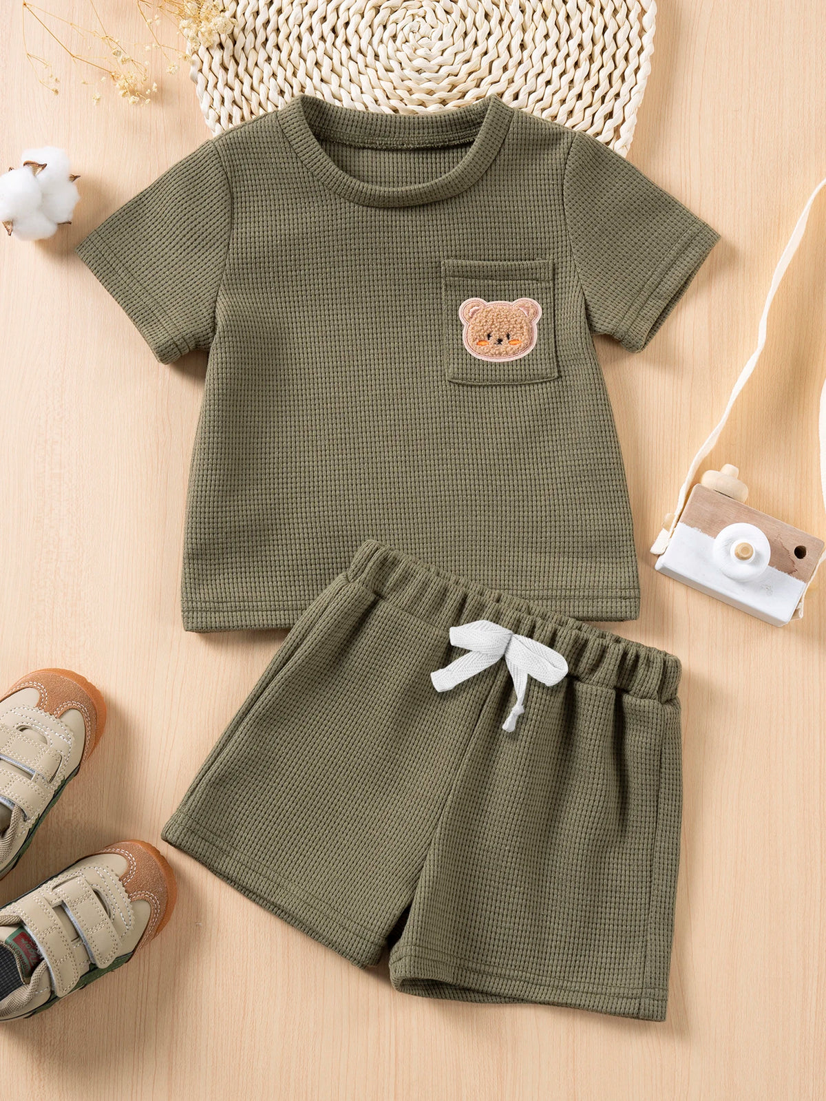 A set of olive green baby clothing featuring a short-sleeved t-shirt with a bear print and matching shorts.
