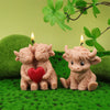 A set of four silicone candle molds shaped like Highland cows sitting on green grass with lit candles.