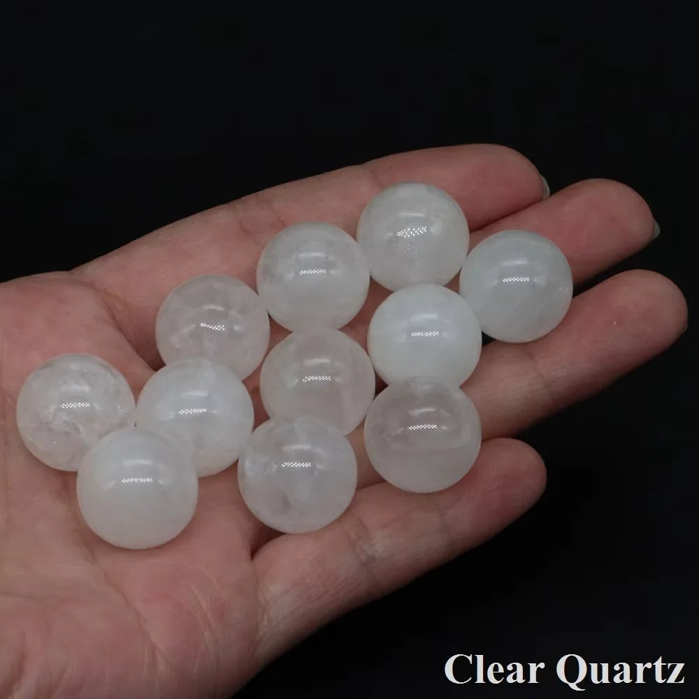 A hand holds several clear quartz spheres of varying sizes and translucency.