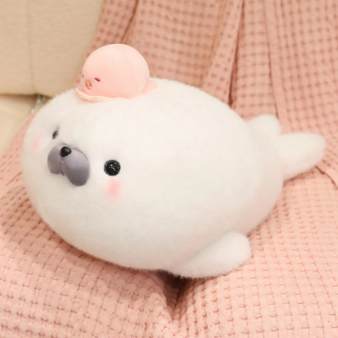 A white seal plush toy with a pink octopus hat resting on a pink textured fabric.