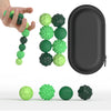 A hand holds a line of green and dark green silicone fidget balls next to a black storage case and several loose balls.