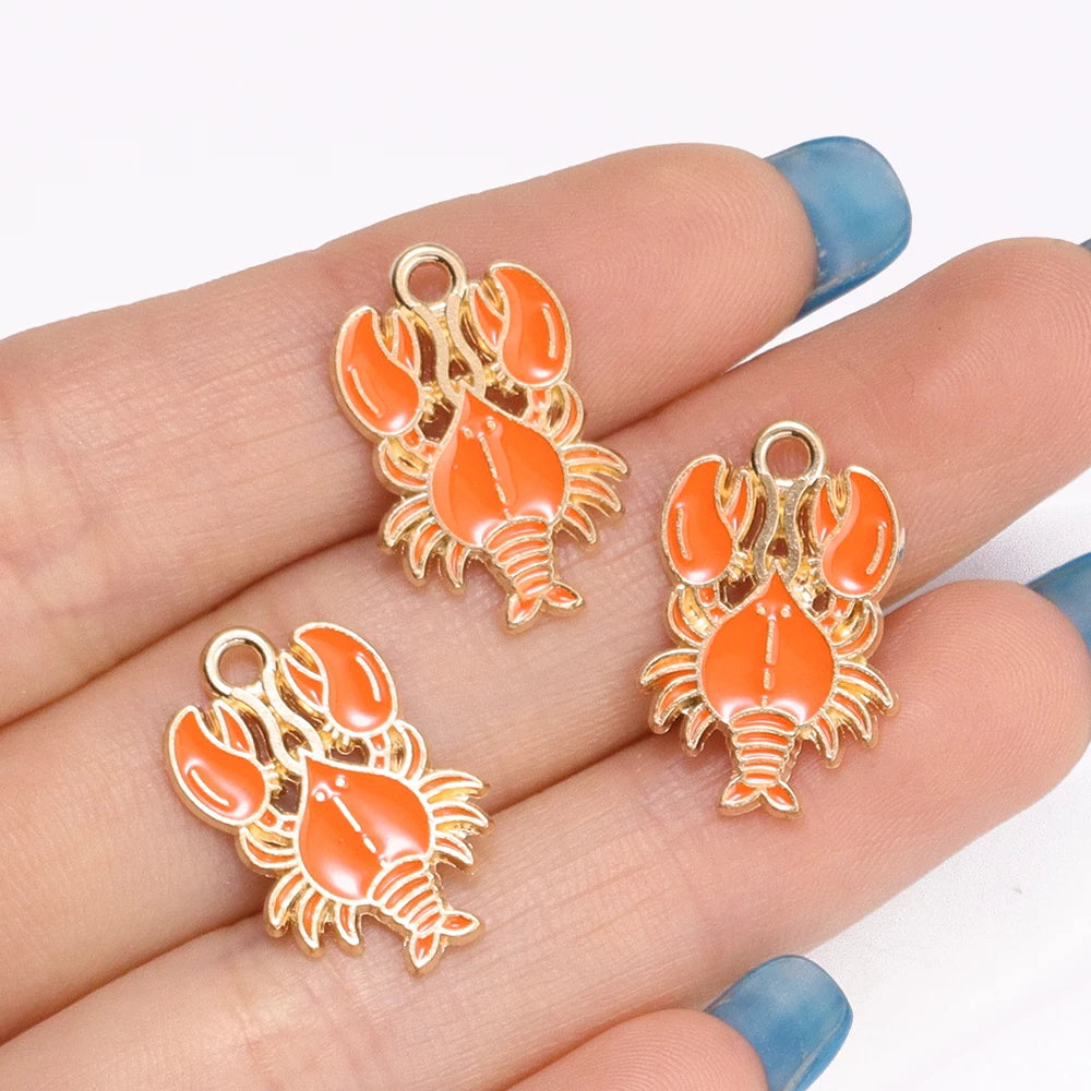 Gold-toned enamel charms shaped like orange shrimp and crab claws displayed on a hand.