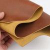 A piece of rust red Crazy Horse leather hide rolled and folded, showing the oily finish and handmade texture.