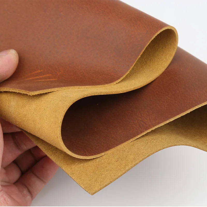 A piece of rust red Crazy Horse leather hide rolled and folded, showing the oily finish and handmade texture.