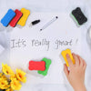 A hand is writing 'It's really great!' on a white sheet with several colorful magnetic dry erase erasers and a black pen.