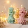 A pair of silicone molds shaped like praying angels in mint green and pink are displayed with glowing fairy lights.