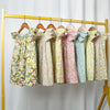 A display of girls floral smocked summer dresses with flying sleeves hanging on a yellow rack.
