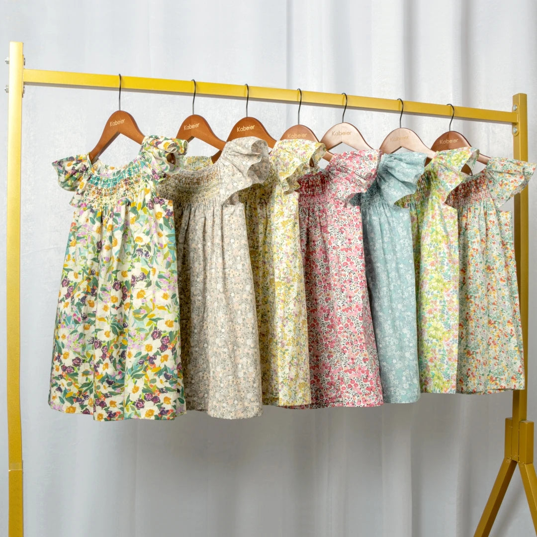 A display of girls floral smocked summer dresses with flying sleeves hanging on a yellow rack.
