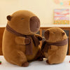 A brown plush capybara stuffed animal wearing a brown knit scarf sitting on a white surface.