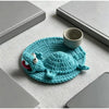 Handmade crochet lizard coaster in teal color resting on a light gray surface with a small ceramic cup.