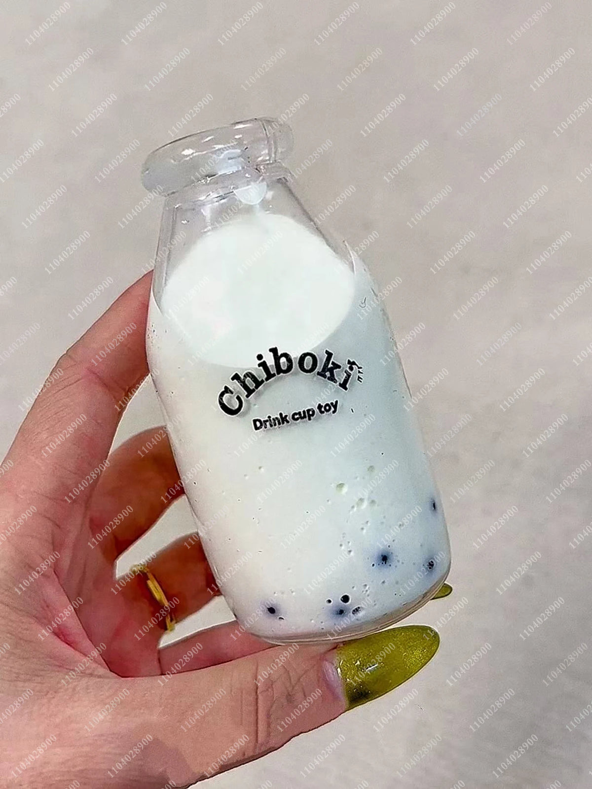 A hand holds a clear bottle filled with white liquid and dark specks, labeled Chiboki Drink cup toy.