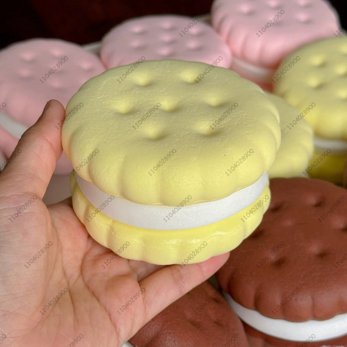 A hand holds a yellow cake squishy fidget toy with white layers, surrounded by other pink and yellow squishies.
