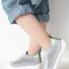 A close-up of a child's foot wearing gray breathable mesh slip-on sneakers with lime green accents.