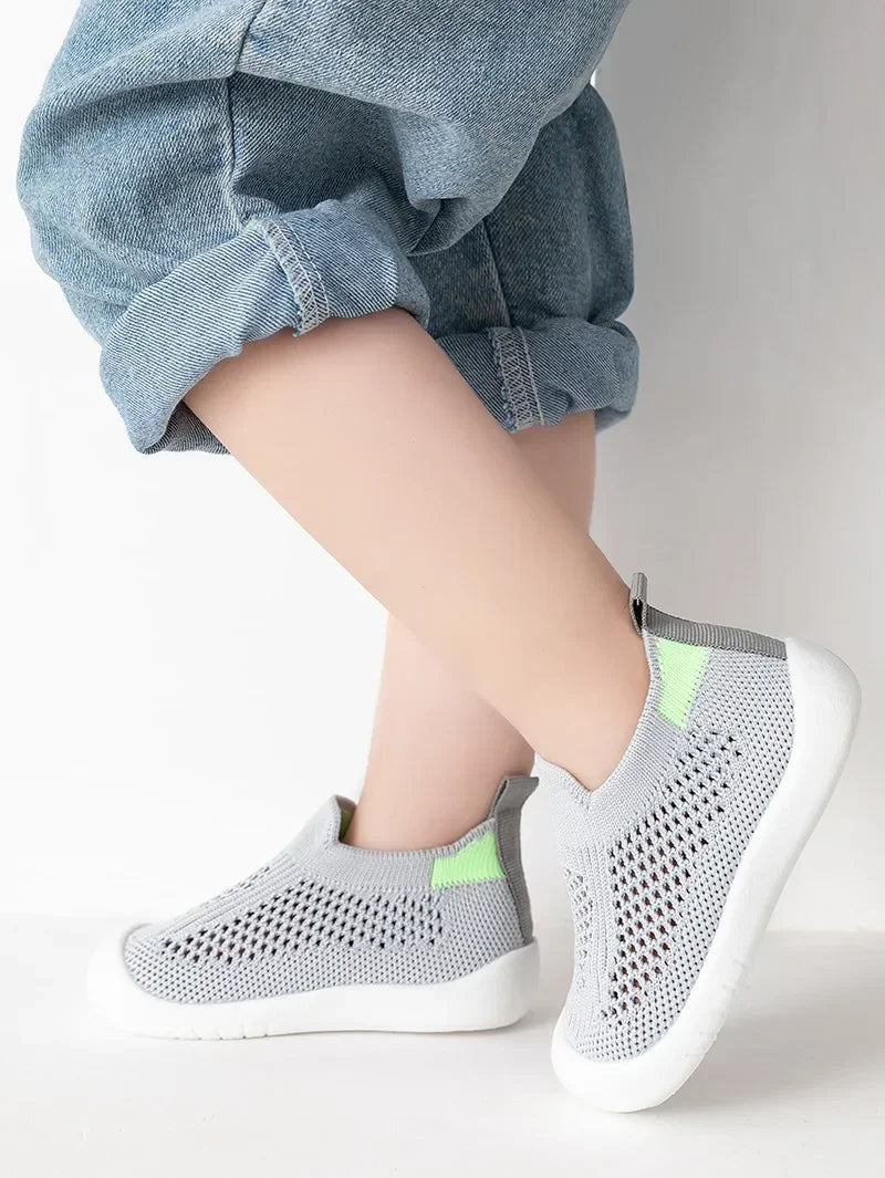A close-up of a child's foot wearing gray breathable mesh slip-on sneakers with lime green accents.