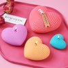 A set of three silicone heart-shaped candles in pink, purple, and yellow resting on a pink tray.