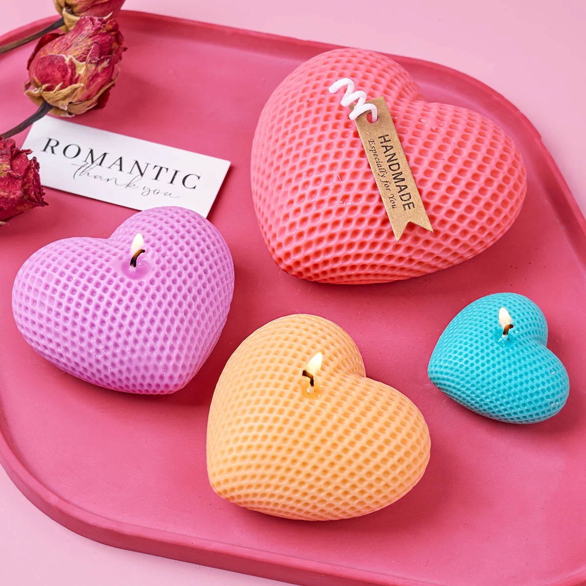 A set of three silicone heart-shaped candles in pink, purple, and yellow resting on a pink tray.