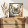 A framed watercolor painting of a butterfly in various shades of blue, green, and orange, displayed on a wooden dresser.