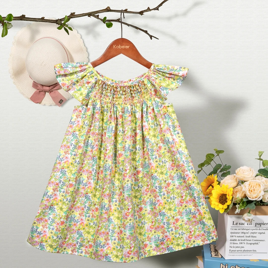 A yellow and pink floral smocked summer dress for girls with flying sleeves displayed on a hanger.