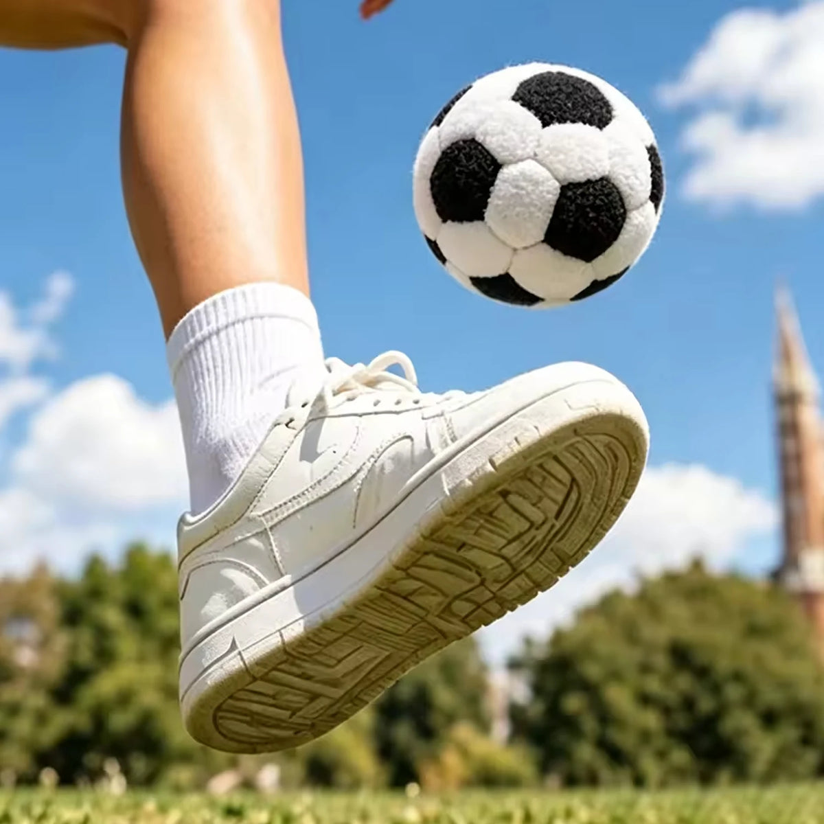 A close-up shot of a foot kicking a black and white soccer ball in mid-air against a blue sky.