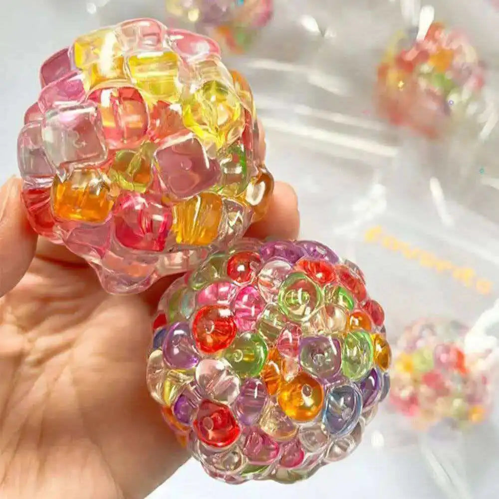 Eine Hand hält einen farbenfrohen, durchsichtigen Fidget-Eiswürfel zum Stressabbau mit rosa, gelben und grünen Tönen.