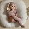 A baby wearing a pink rabbit romper set with a matching hat and socks, lying on a white textured surface.