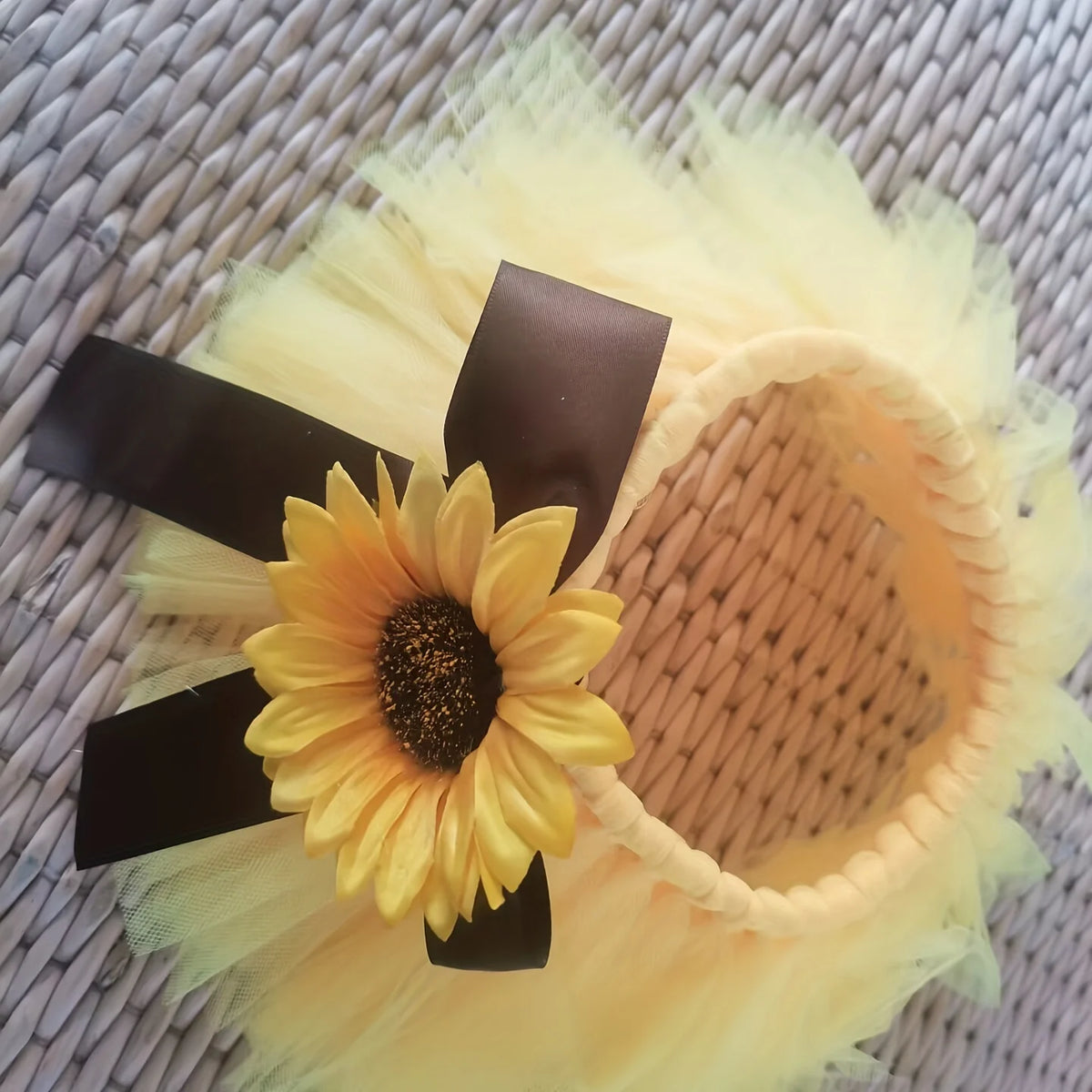 A yellow sunflower decoration with black ribbon is placed on a sheer yellow tulle fabric background.