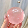 A hand holds a large, translucent pink coconut oil squishy stress relief ball against a light background.