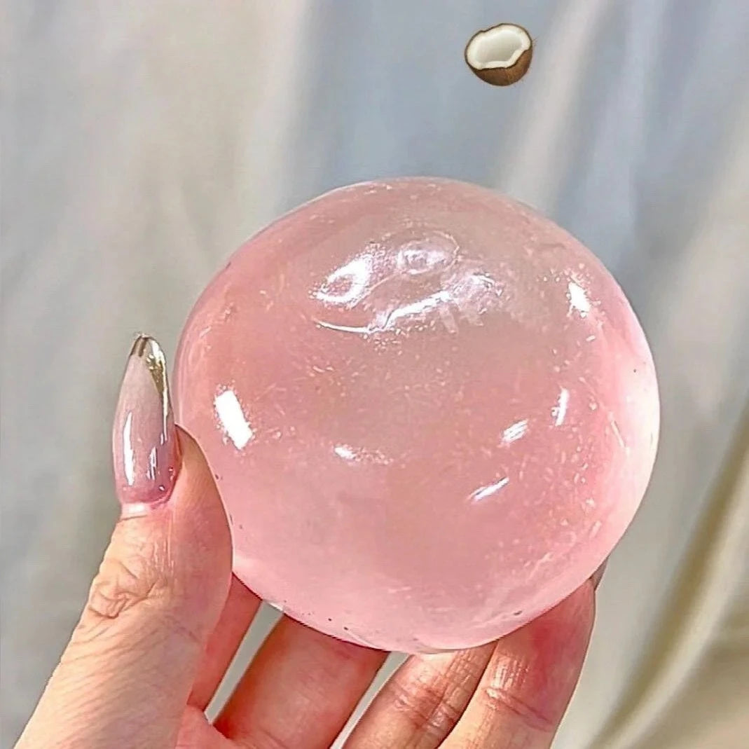 A hand holds a large, translucent pink coconut oil squishy stress relief ball against a light background.