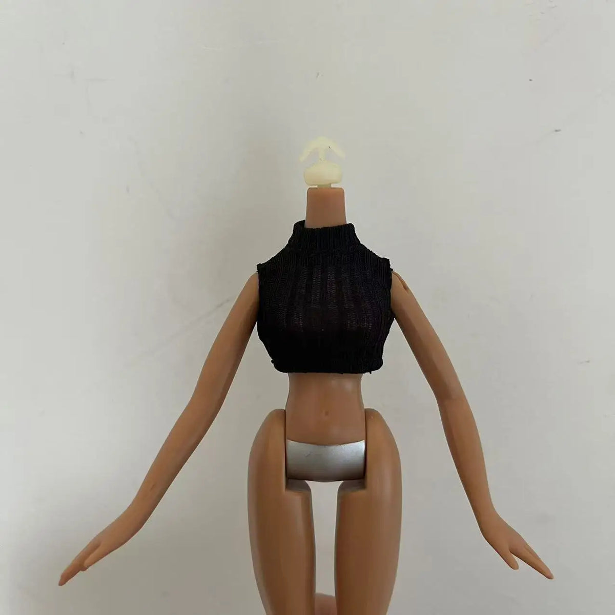 A fashion doll with light blonde hair wearing a black knitted top and silver bottoms.