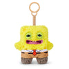 A yellow plush monster with large eyes and a mouth, wearing a brown outfit, attached to a wooden keychain.