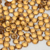 A close-up view of small, round, golden-yellow glass crystal flatback rhinestones scattered on a white surface.