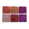 A clear plastic tray containing four compartments of glitter in shades of copper, gold, magenta, and purple.