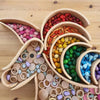 A collection of natural wooden rainbow building blocks in various colors and shapes arranged in wooden bowls.