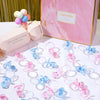 A collection of mini acrylic pacifier party favors in various shades of pink and blue are displayed on a white surface.